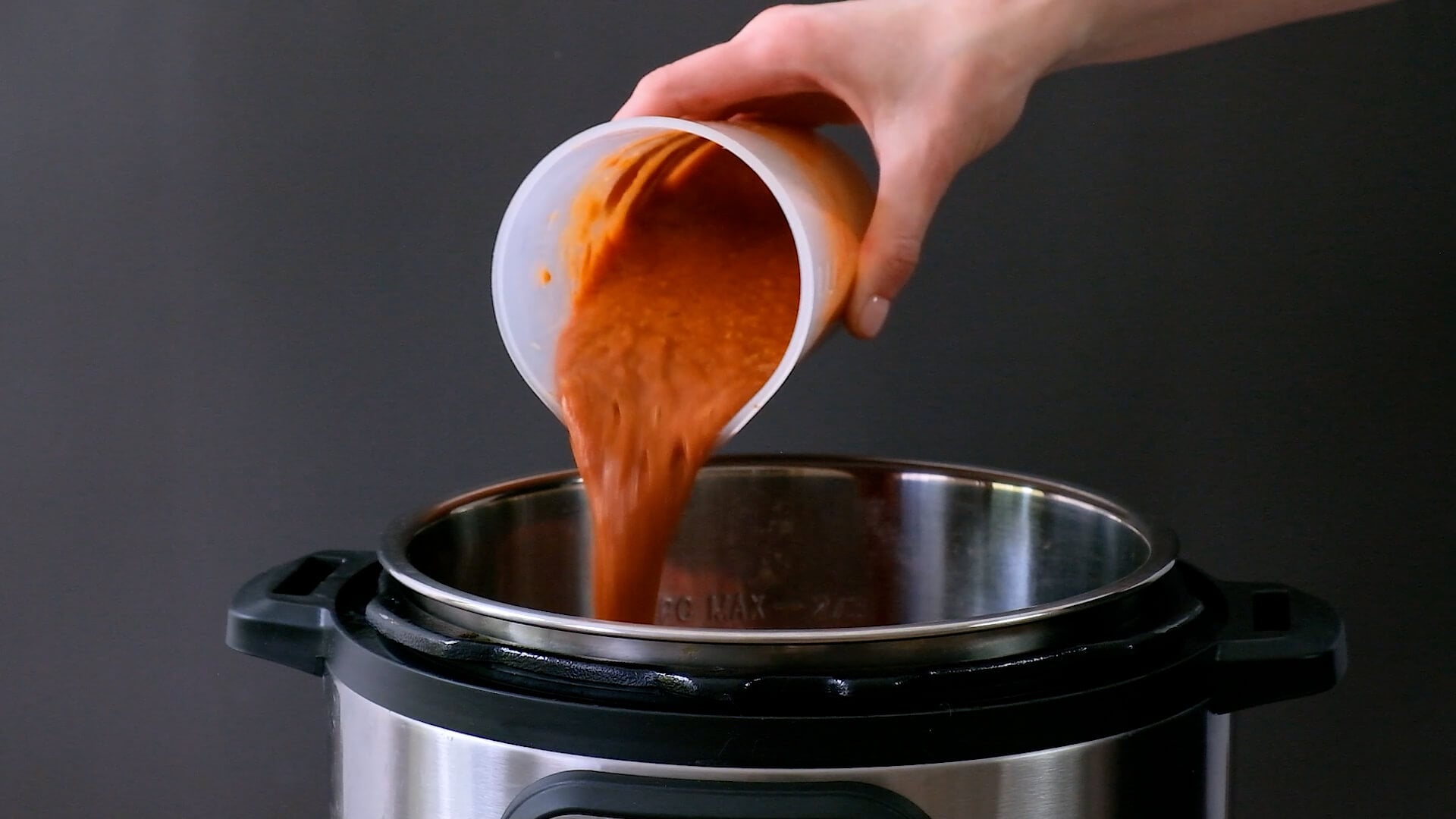 Pouring homemade BBQ sauce in a slow cooker over onions and pork shoulder.