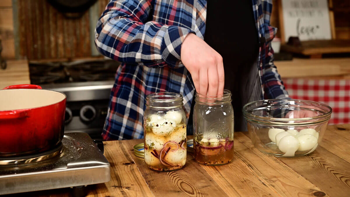 A girl adding hard boiled eggs to a jar of brine.