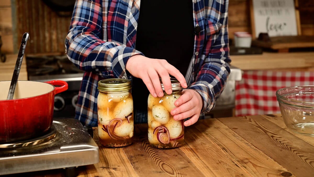 A girl screwing a lid onto a jar of pickled eggs.