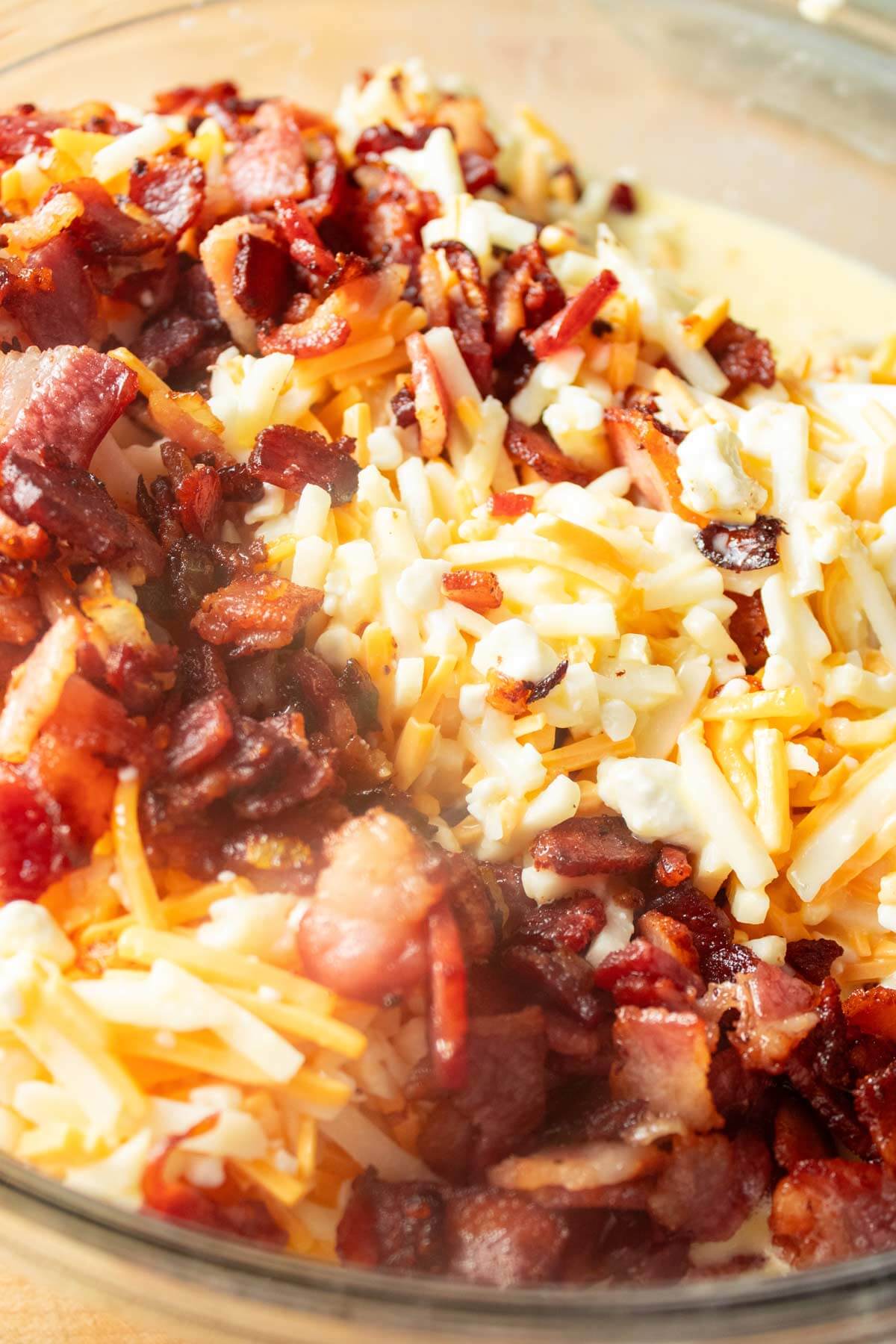 Amish breakfast casserole ingregients (cottage cheese, cheddar cheese, bacon, onion, potatoes, and eggs) mixing in a bowl.