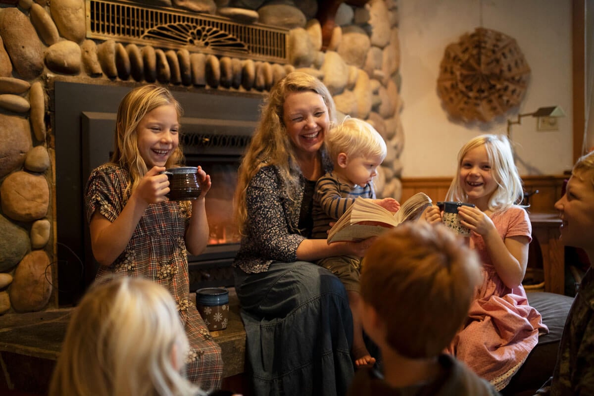 A mom reading to her children by a fireplace.