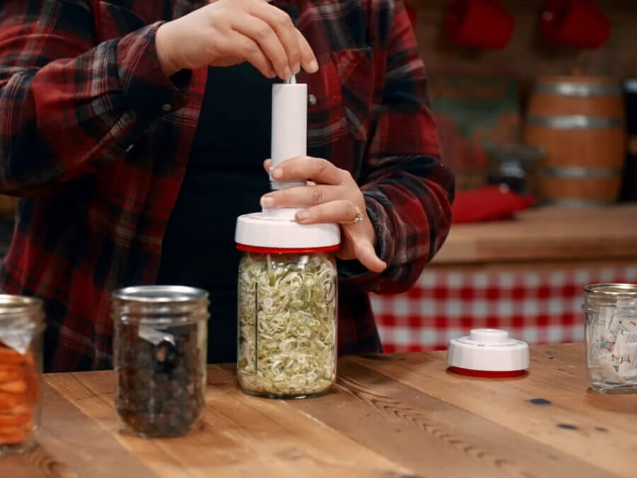 A woman vacuum sealing a jar of freeze dried food with a hand pump.