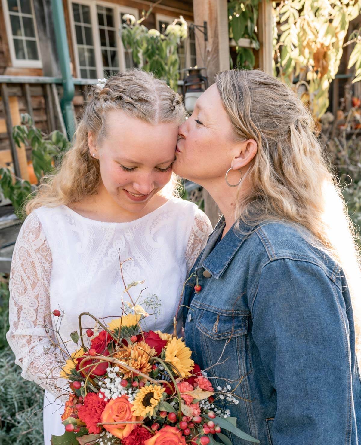 A mother kissing her daughter's cheek on the daughter's wedding day.