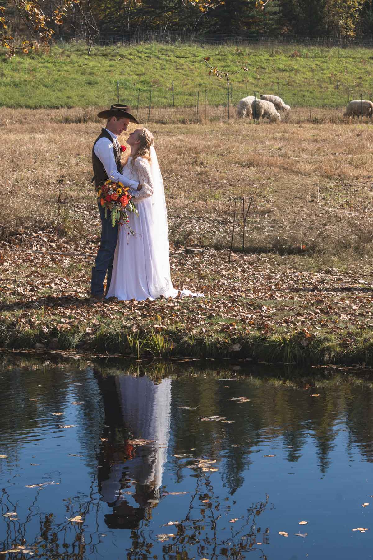 A husband and wife on their wedding day near a pond.