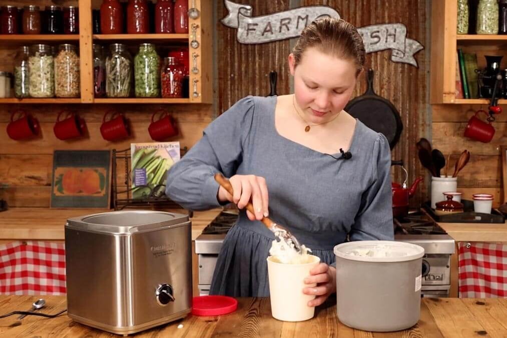 A young girl adding ice cream to a freezer container.
