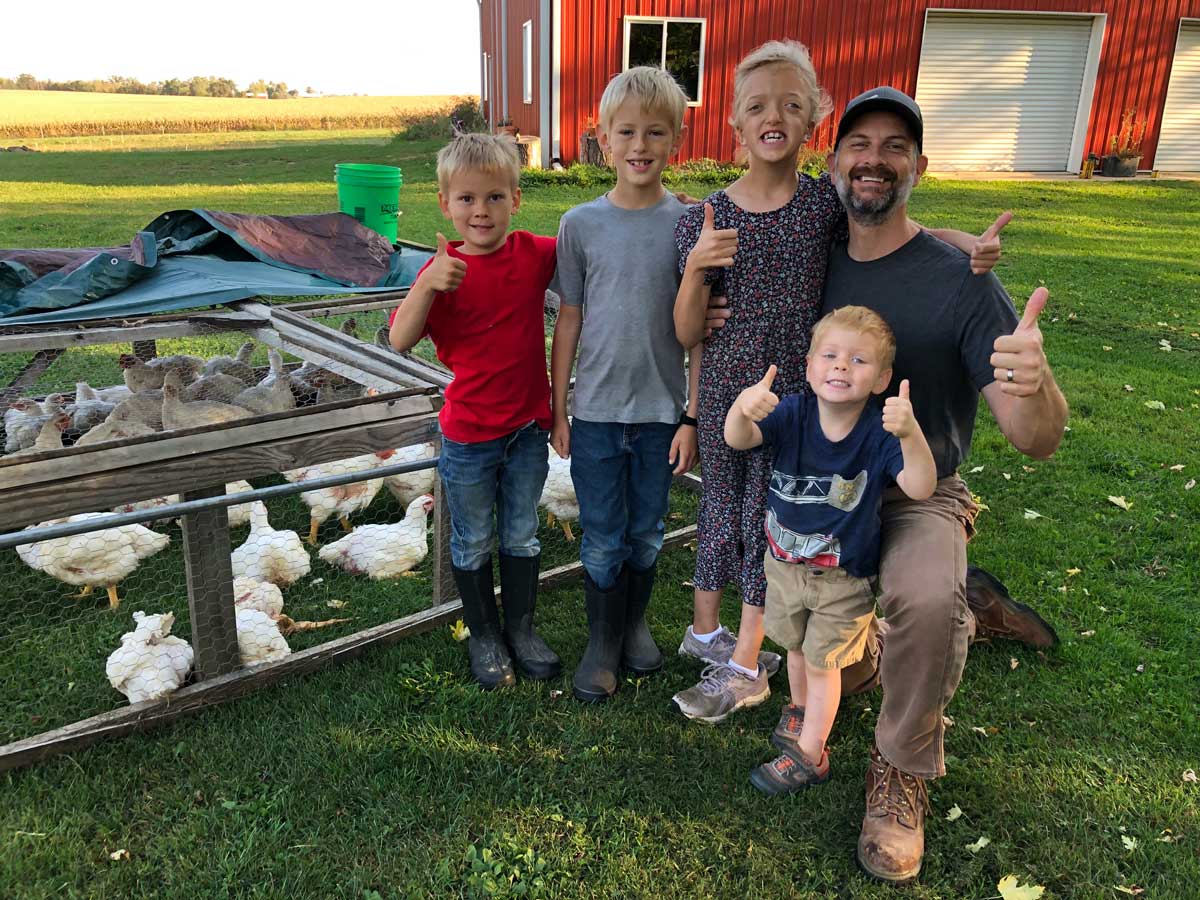 A father with his children next to a chicken tractor with meat birds.