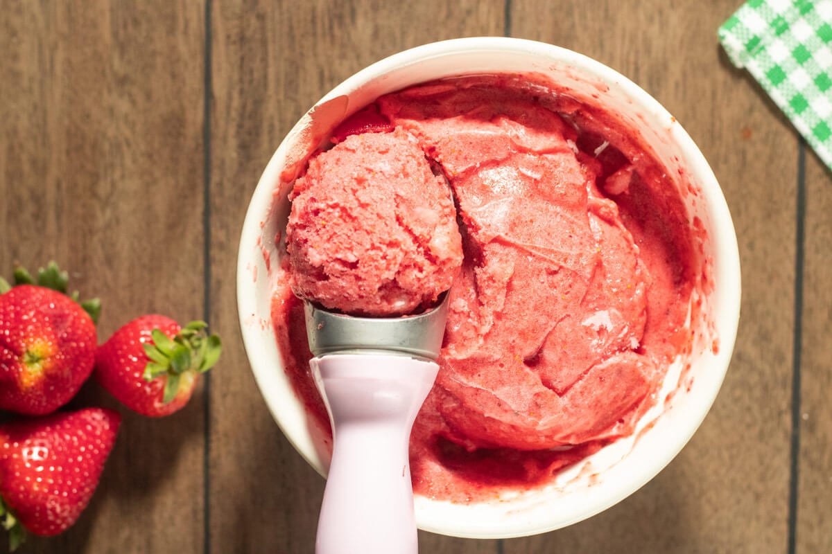 A white bowl filled with strawberry sorbet, and a scoop removing a serving to show texture.