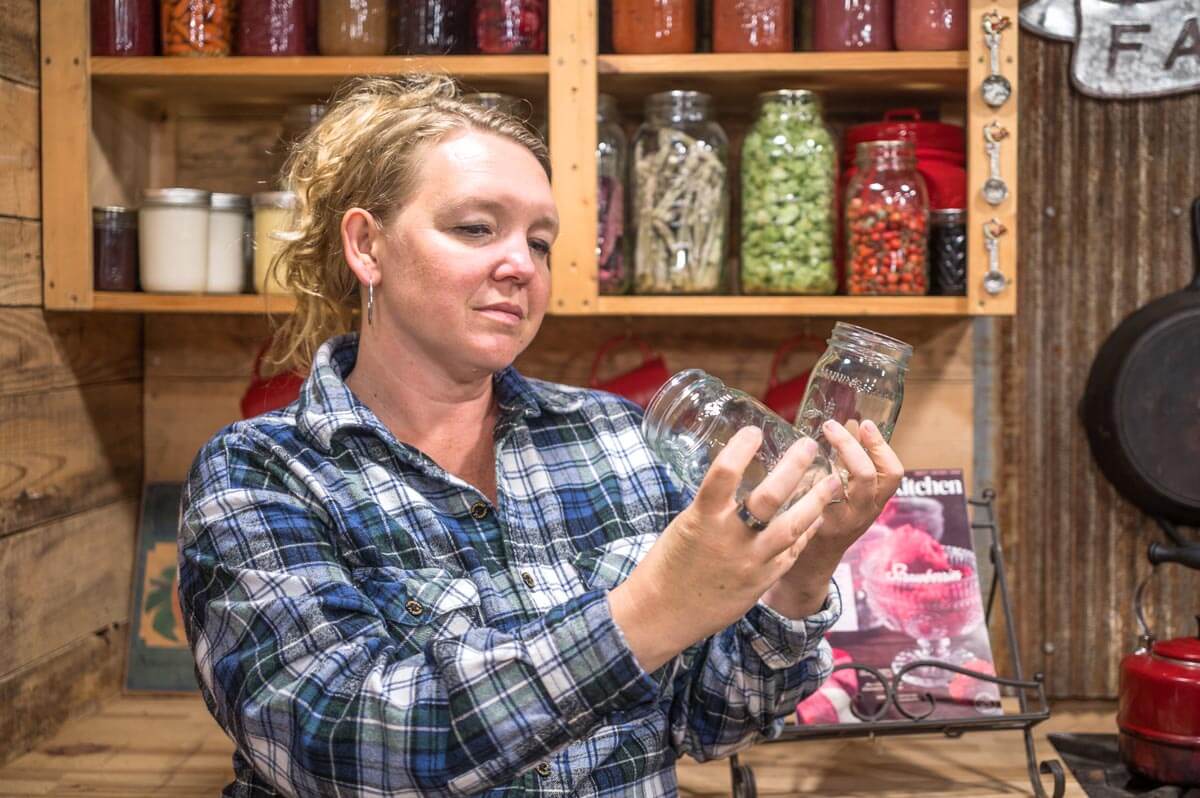 A woman inspecting two canning jars.