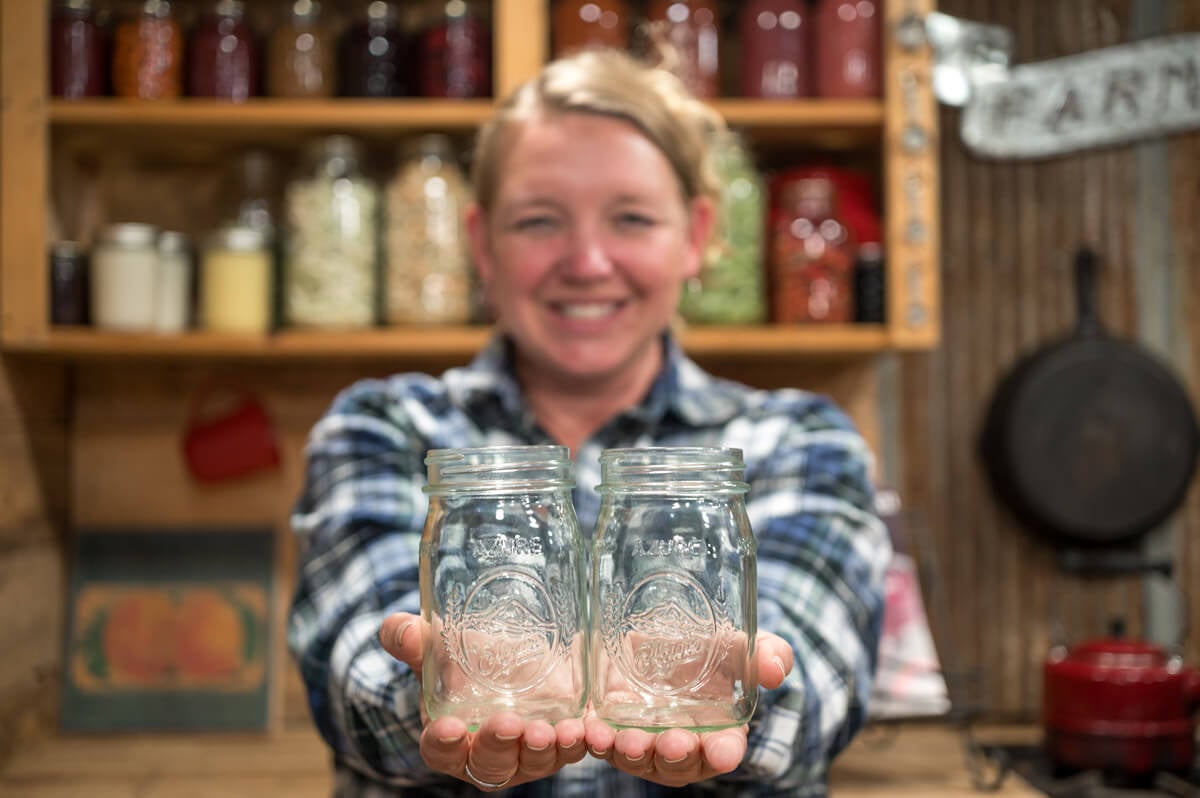 A woman holding out two caning jars.