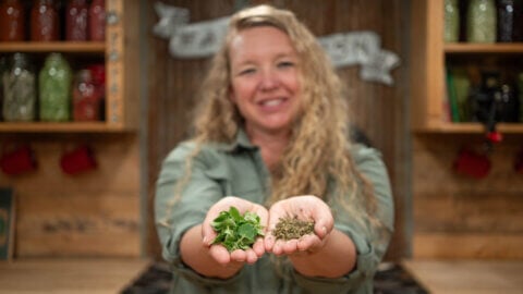 A woman holding dried herbs in one hand and fresh herbs in the other.