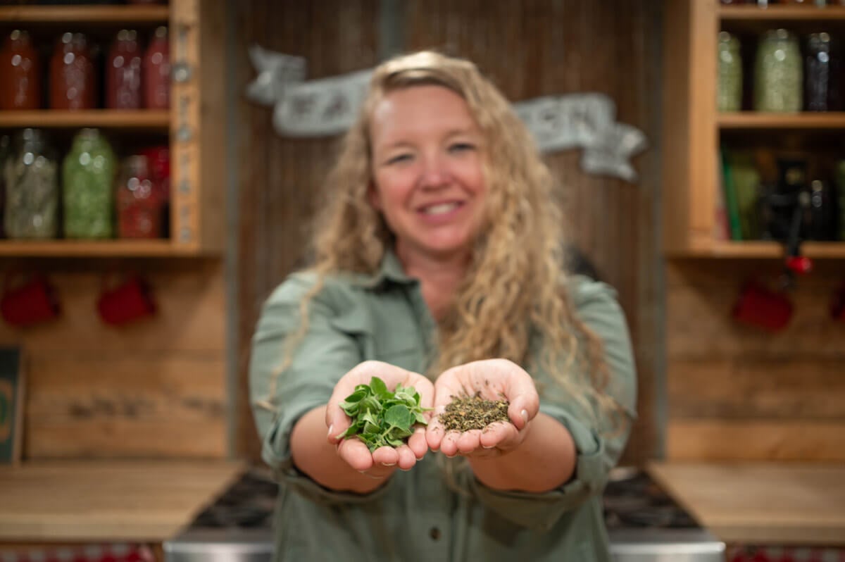 A woman holding dried herbs in one hand and fresh herbs in the other.
