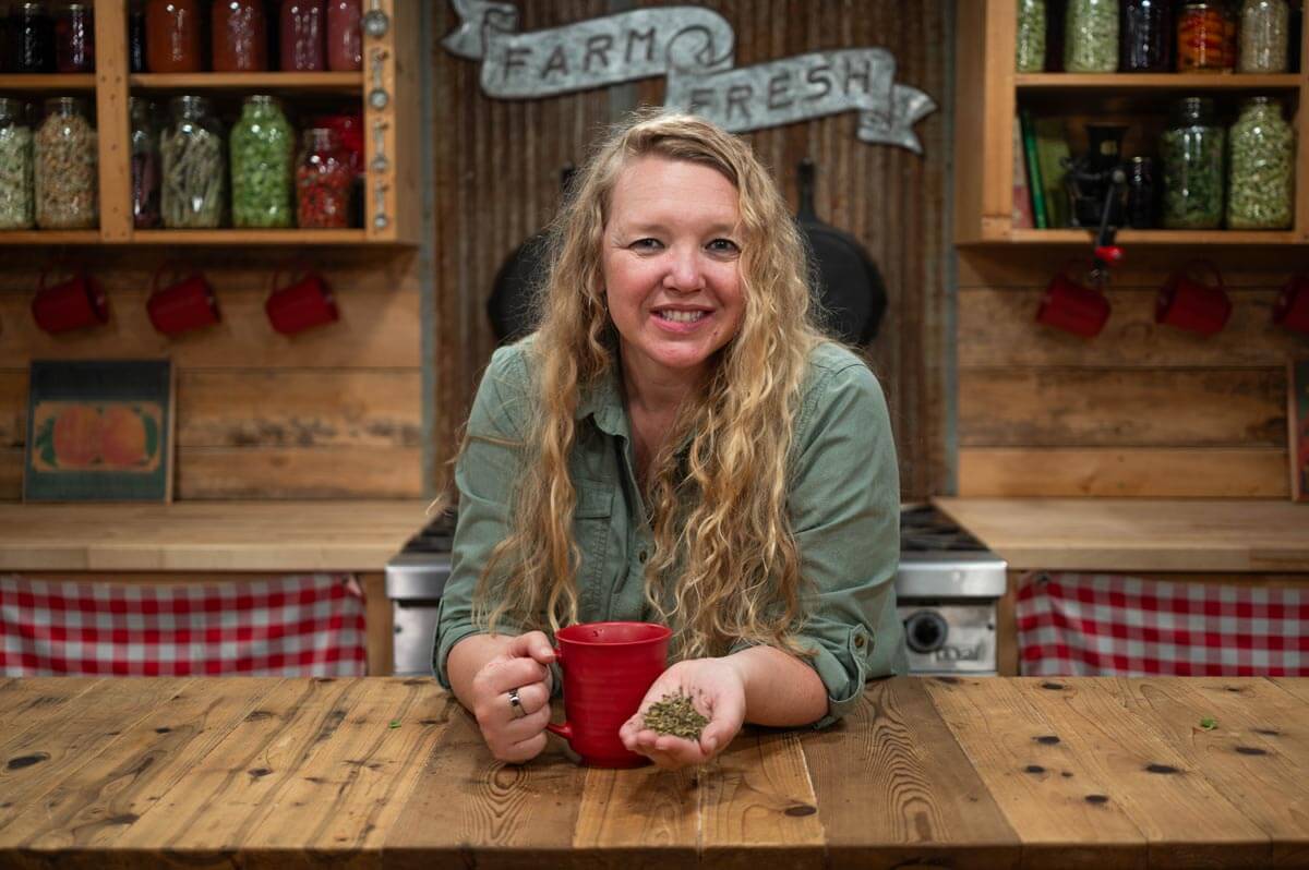 A woman holding a handful of dried herbs and a cup of tea in the other hand.