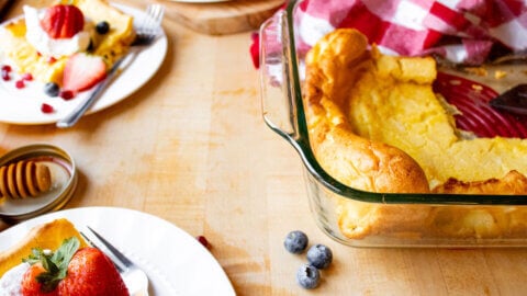 Servings of German pancake on white plates surrounding a baking dish filled with remaining German pancake.