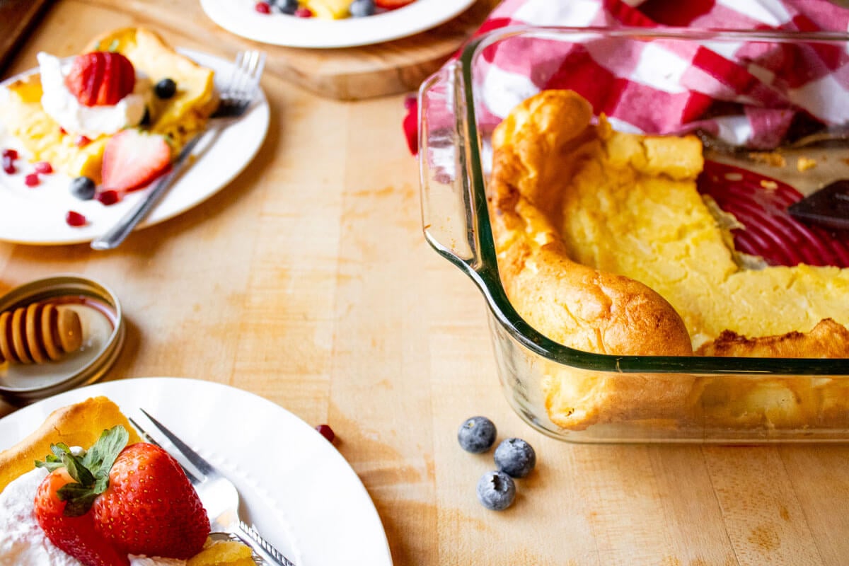 Servings of German pancake on white plates surrounding a baking dish filled with remaining German pancake.