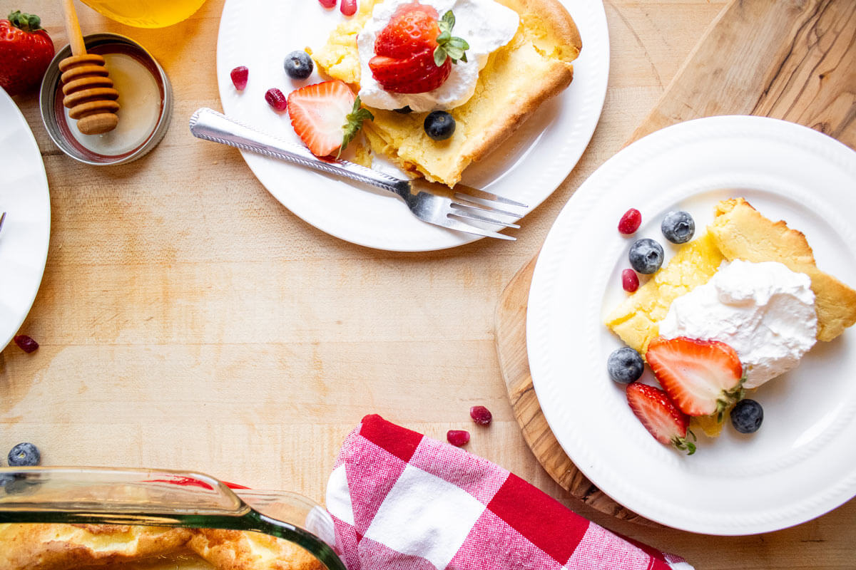 Servings of German pancake garnished with fresh berries and whipped cream.