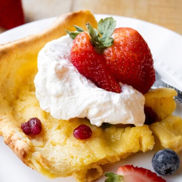 A serving of German pancake garnished with fresh berries and whipped cream.