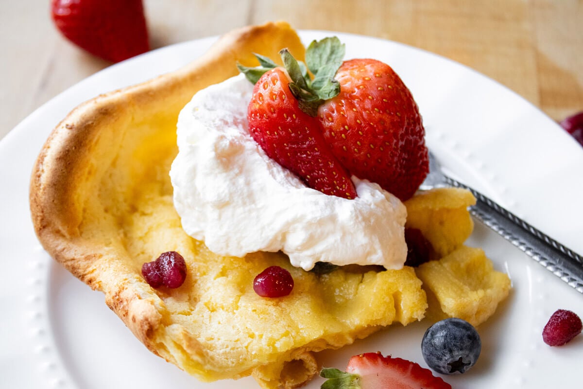 A serving of German pancake garnished with fresh berries and whipped cream.
