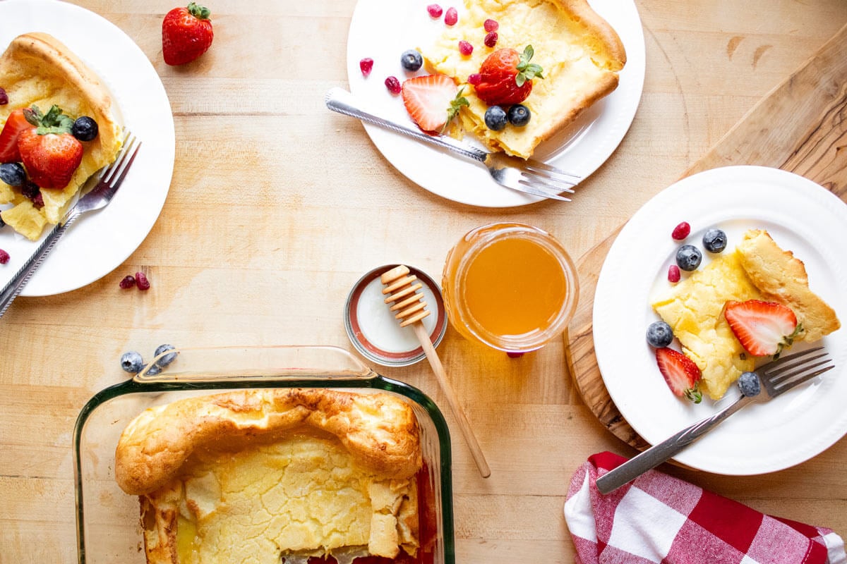 Servings of German pancake on white plates surrounding a baking dish filled with remaining German pancake.