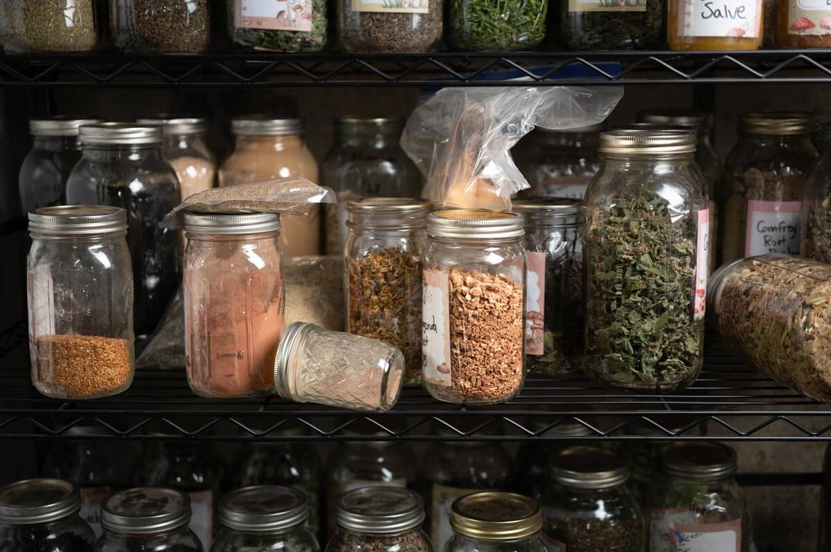 Multiple herbs in jars on a large shelving unit.