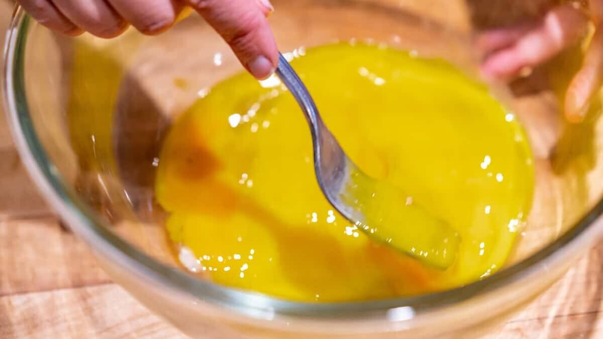 A clear glass bowl with eggs being scrambled with a fork.