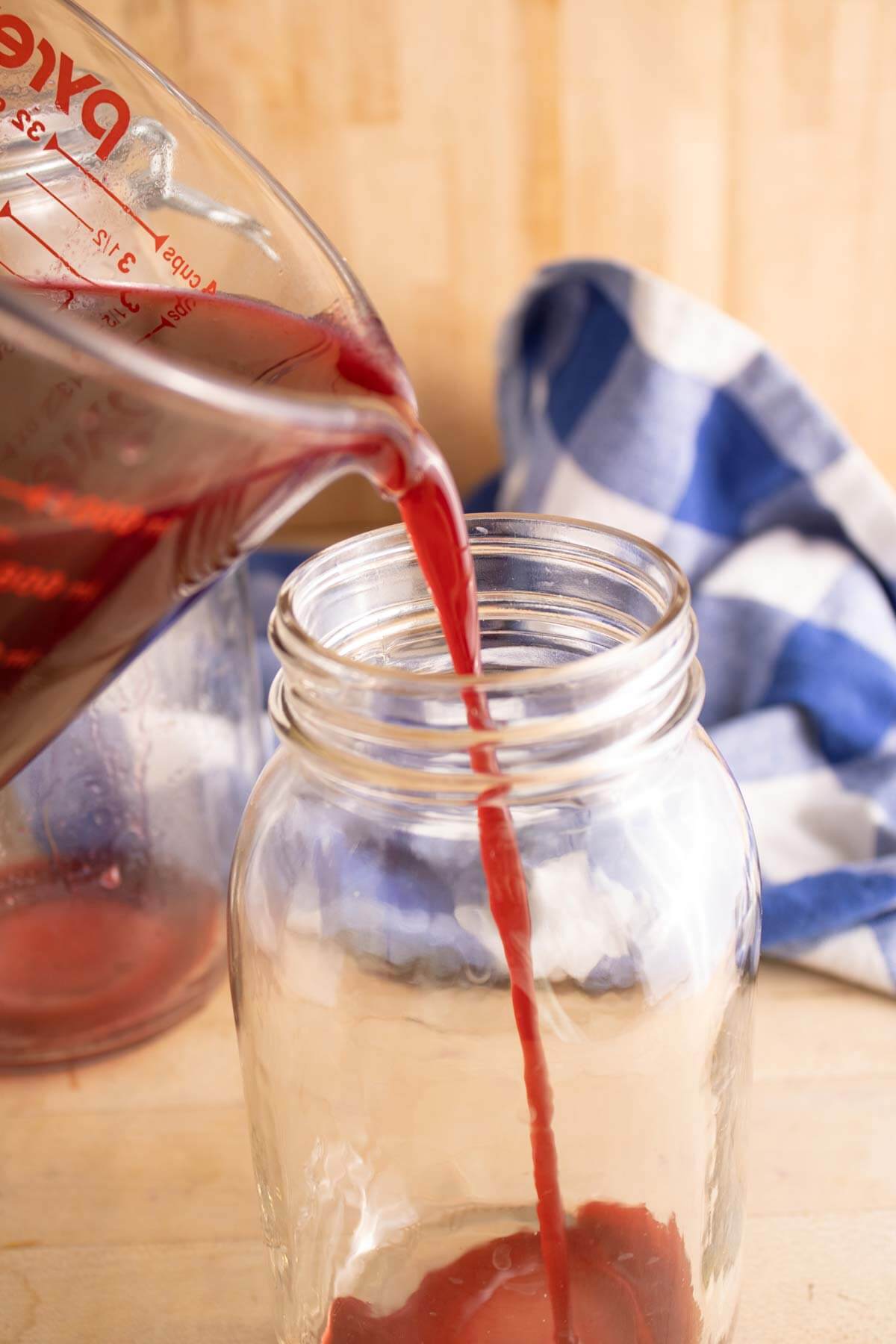 Strained blackberry juice being poured into a jar with apple cider vinegar.