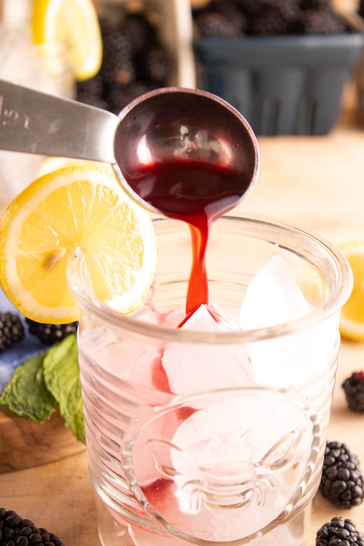 A blackberry shrub syrup being poured over ice into a glass.