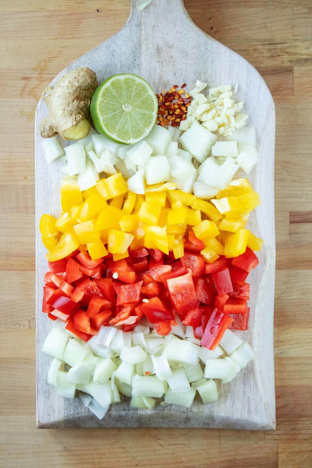 Chopped onions, peppers, ginger, lime, and garlic on a cutting board ready to make fermented pepper sauce.