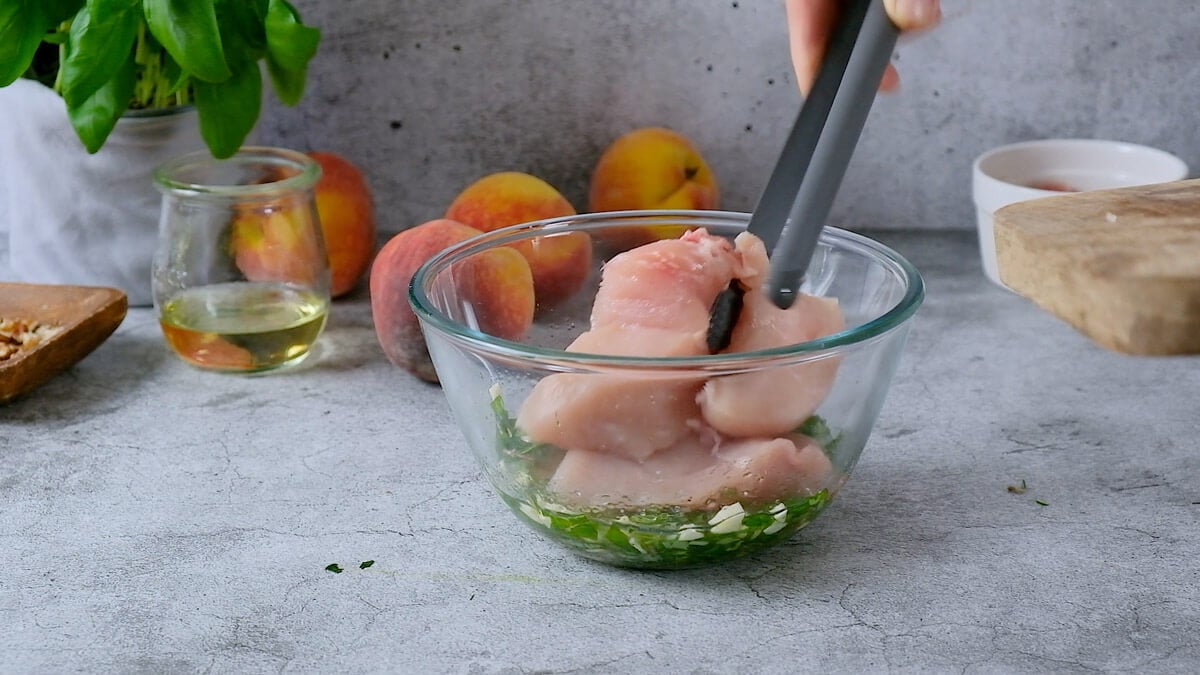 Tongs placing raw chicken breast in a bowl of marinade.
