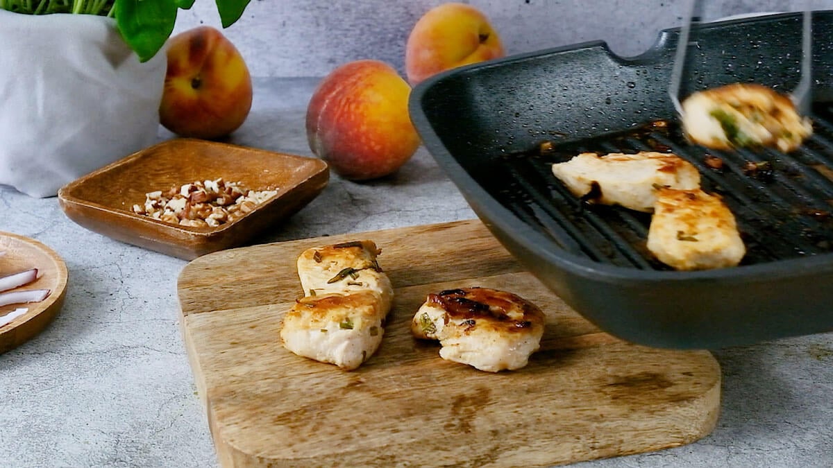 Tongs removing chicken from a cast iron pan to a cutting board.