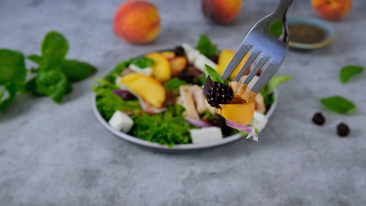 Peach salad with feta on a plate with a fork lifting a bite to show texture.