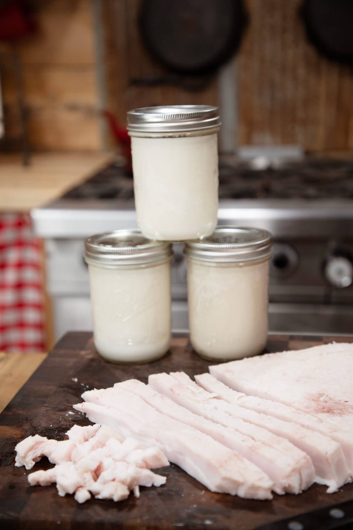 Three jars of finished lard sitting behind leaf lard on a cutting board.