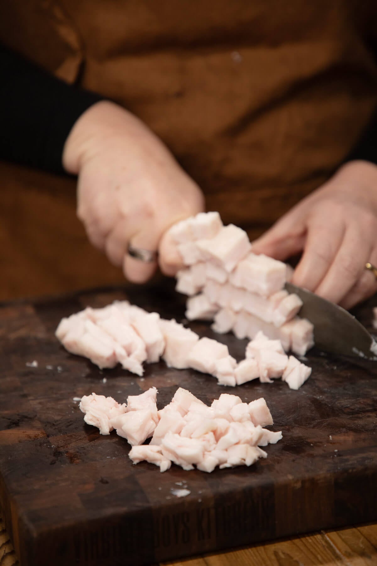 Hands holding a knife chopping leaf lard to prepare for rendering.