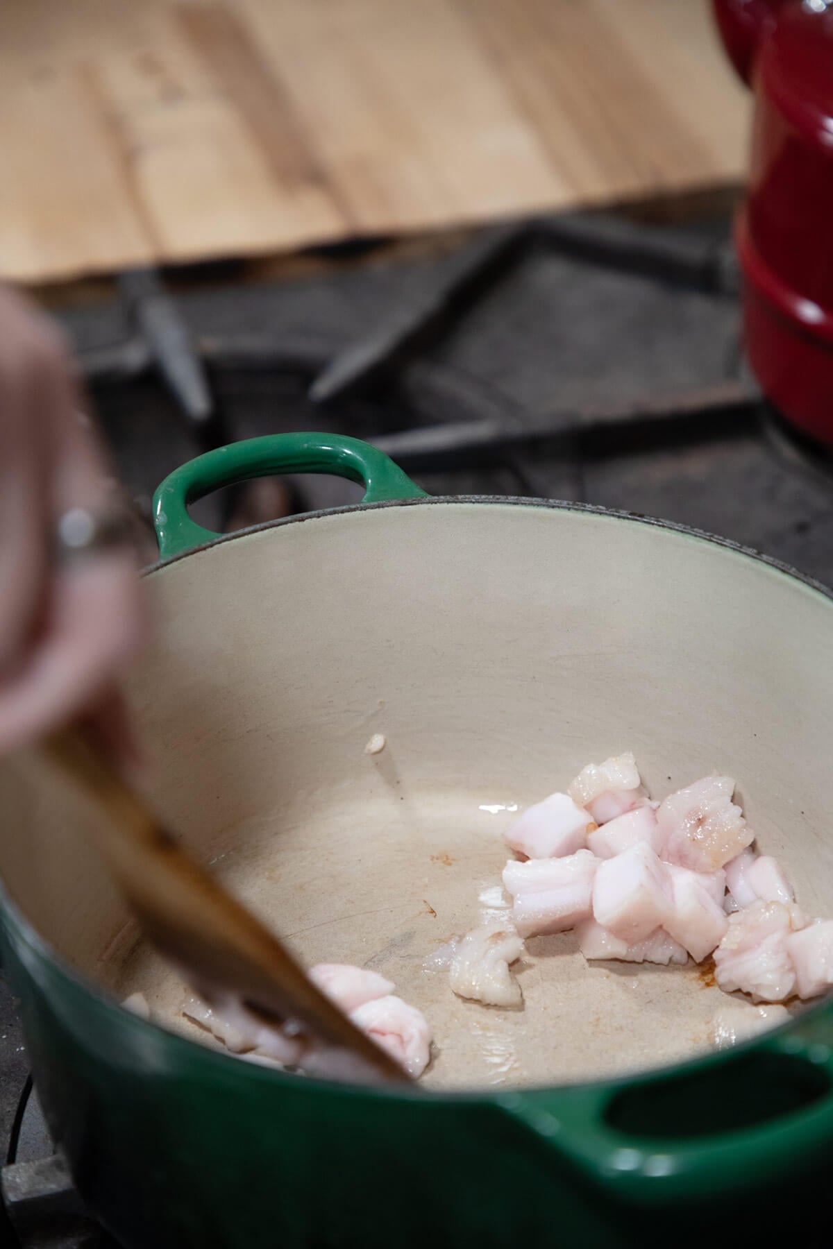 A wooden spoon stirring leaf lard in a Dutch oven.