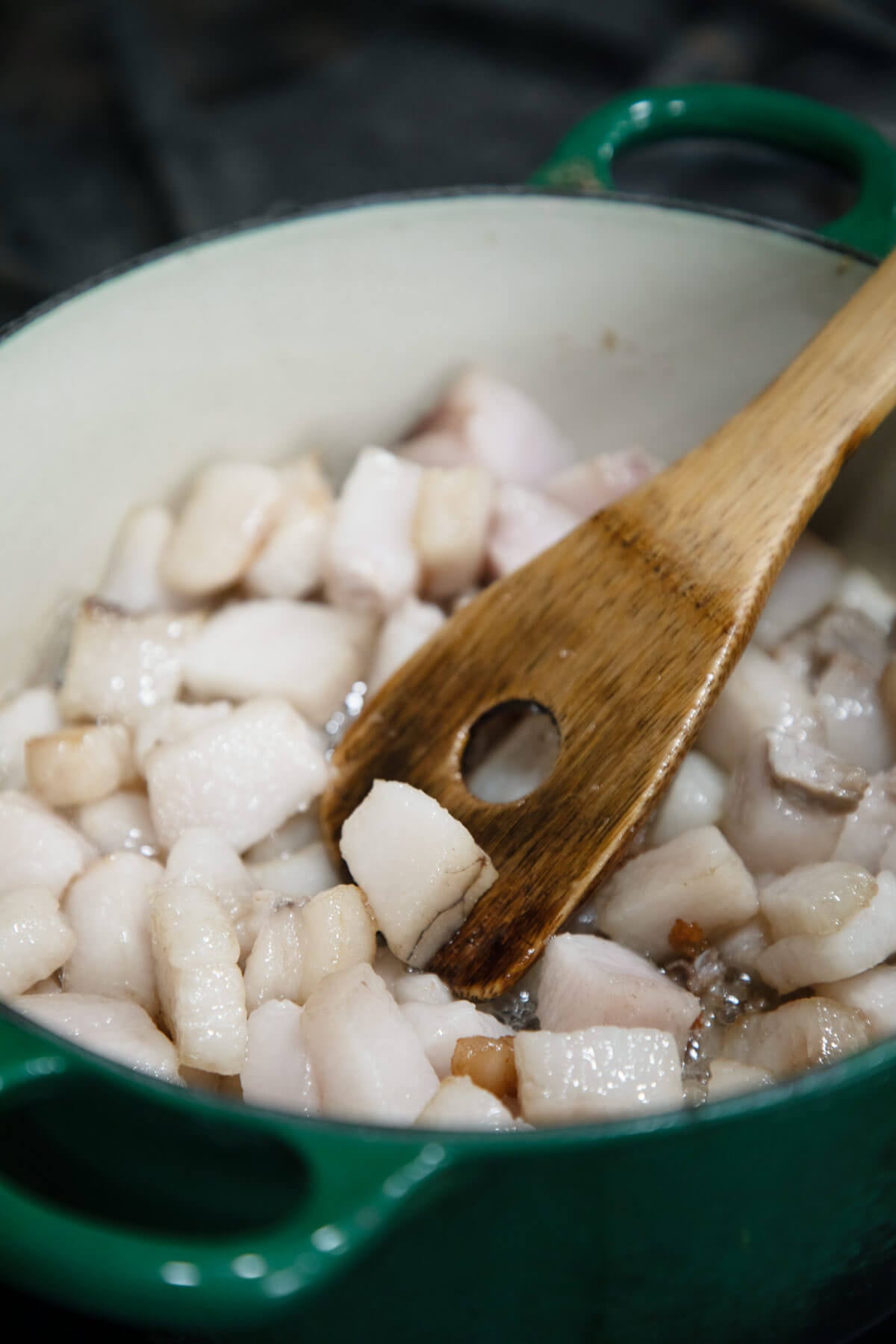 A wooden spoon stirring leaf lard in a Dutch oven.