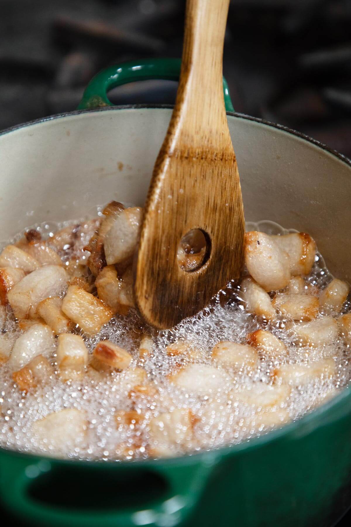 A wooden spoon stirring leaf lard in a Dutch oven.