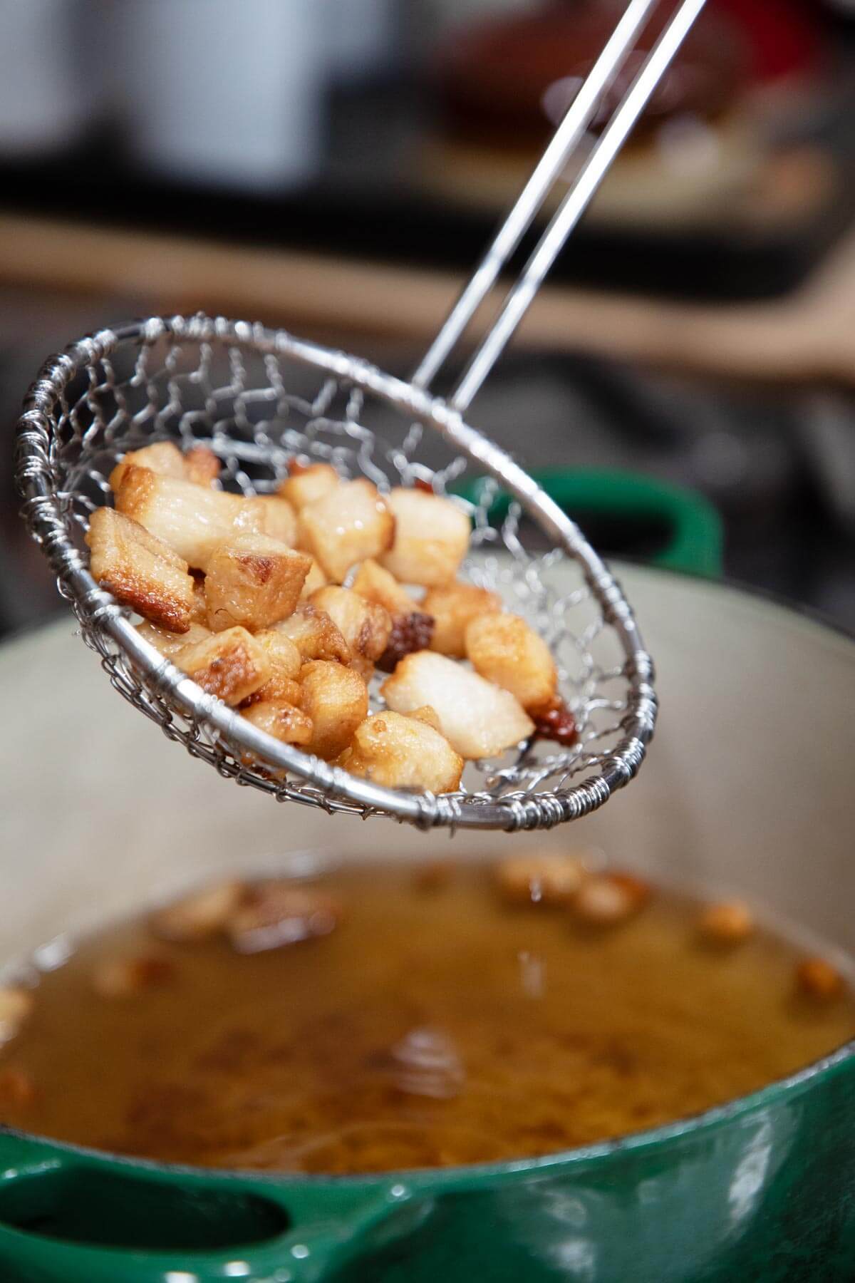A mesh skimmer pulling cracklings out of rendered lard in a Dutch oven.