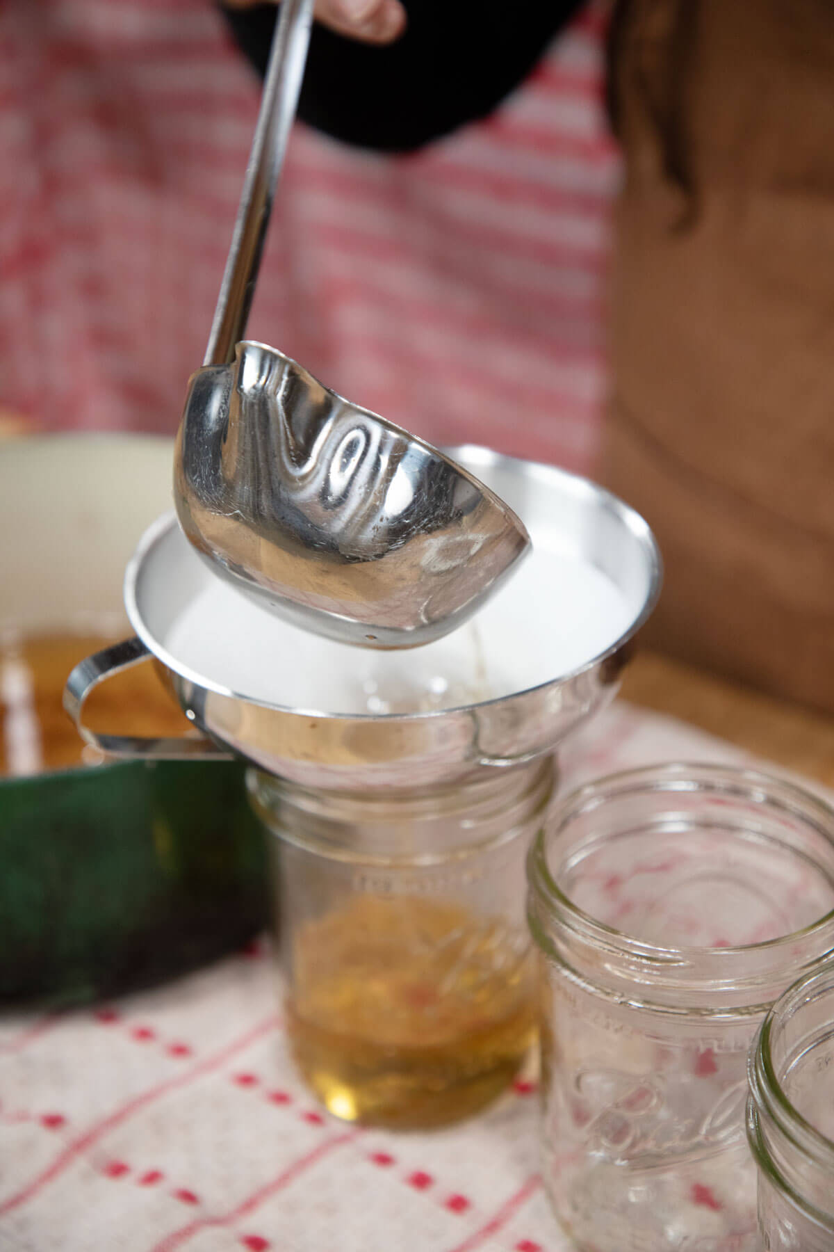 A ladle pouring rendered lard through a funnel into a glass jar.