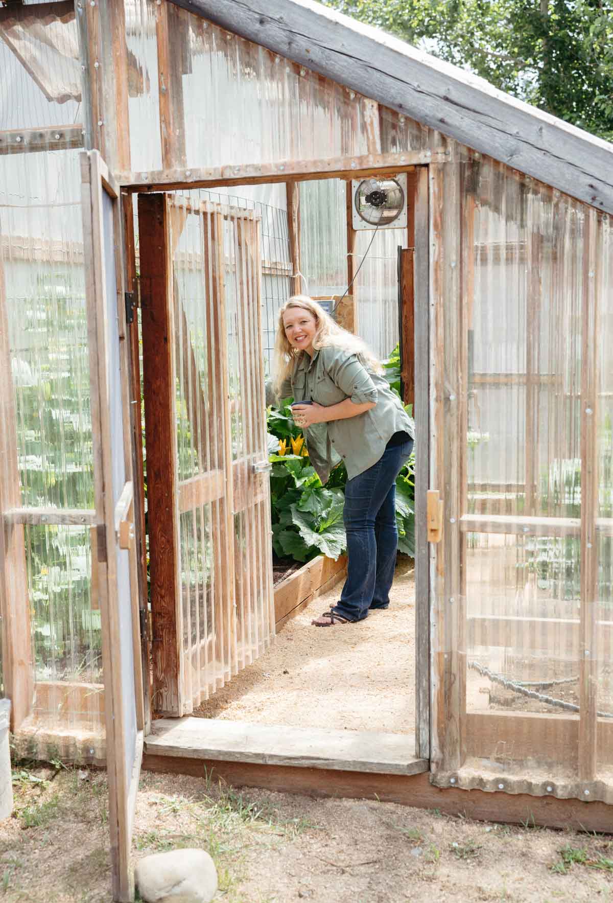 A woman in a greenhouse with a cup of coffee.