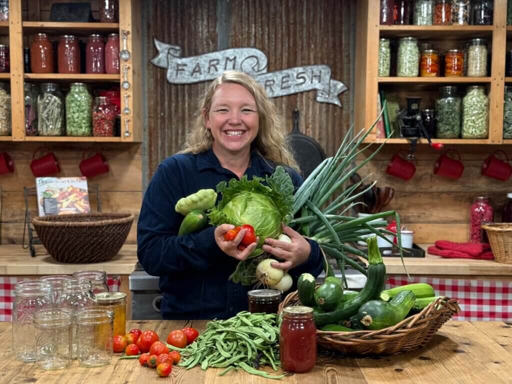 A woman with an armful of produce in the kitchen.