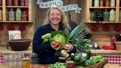 A woman with an armful of produce in the kitchen.