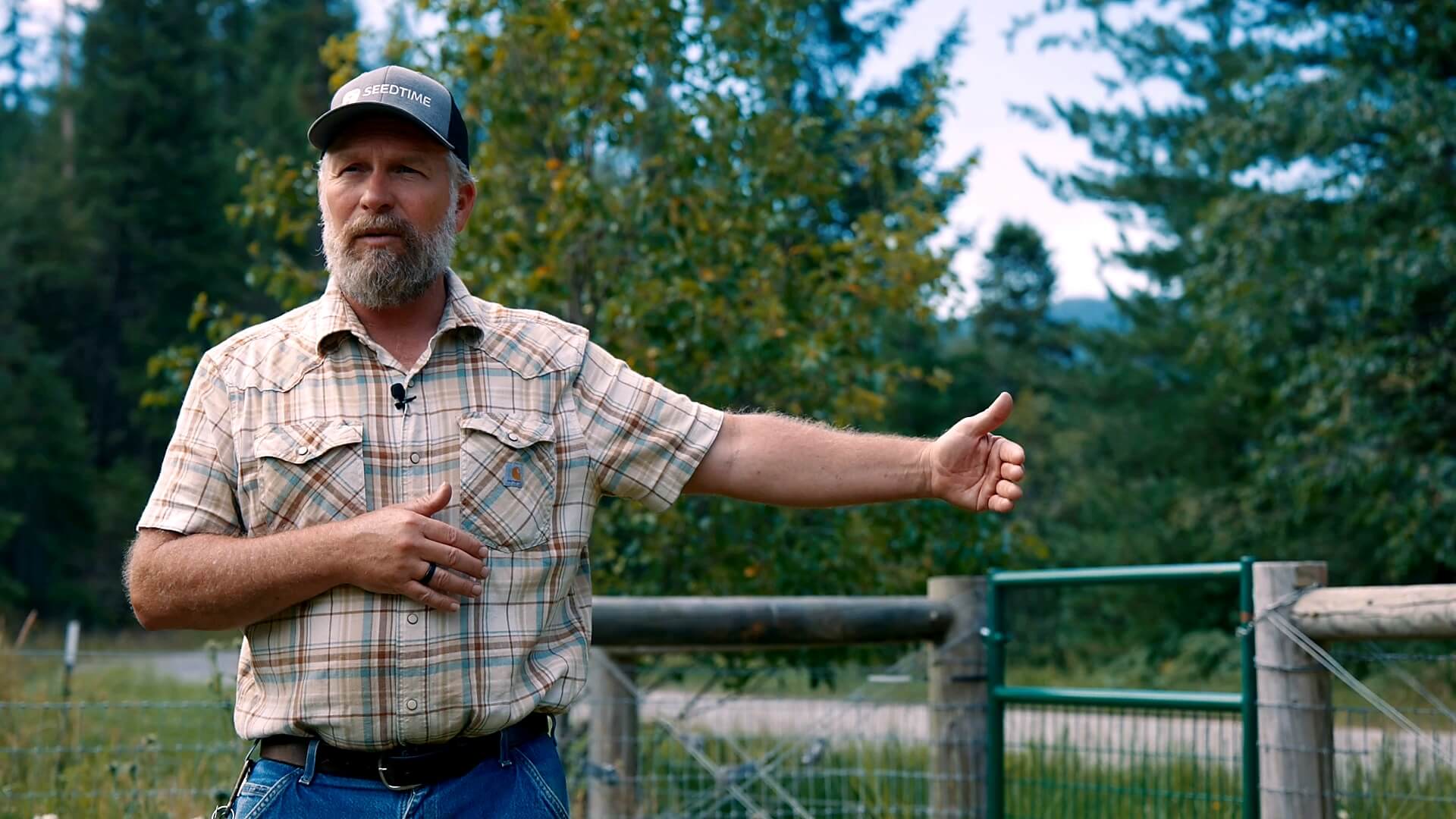 A man standing in a pasture pointing to fencing.