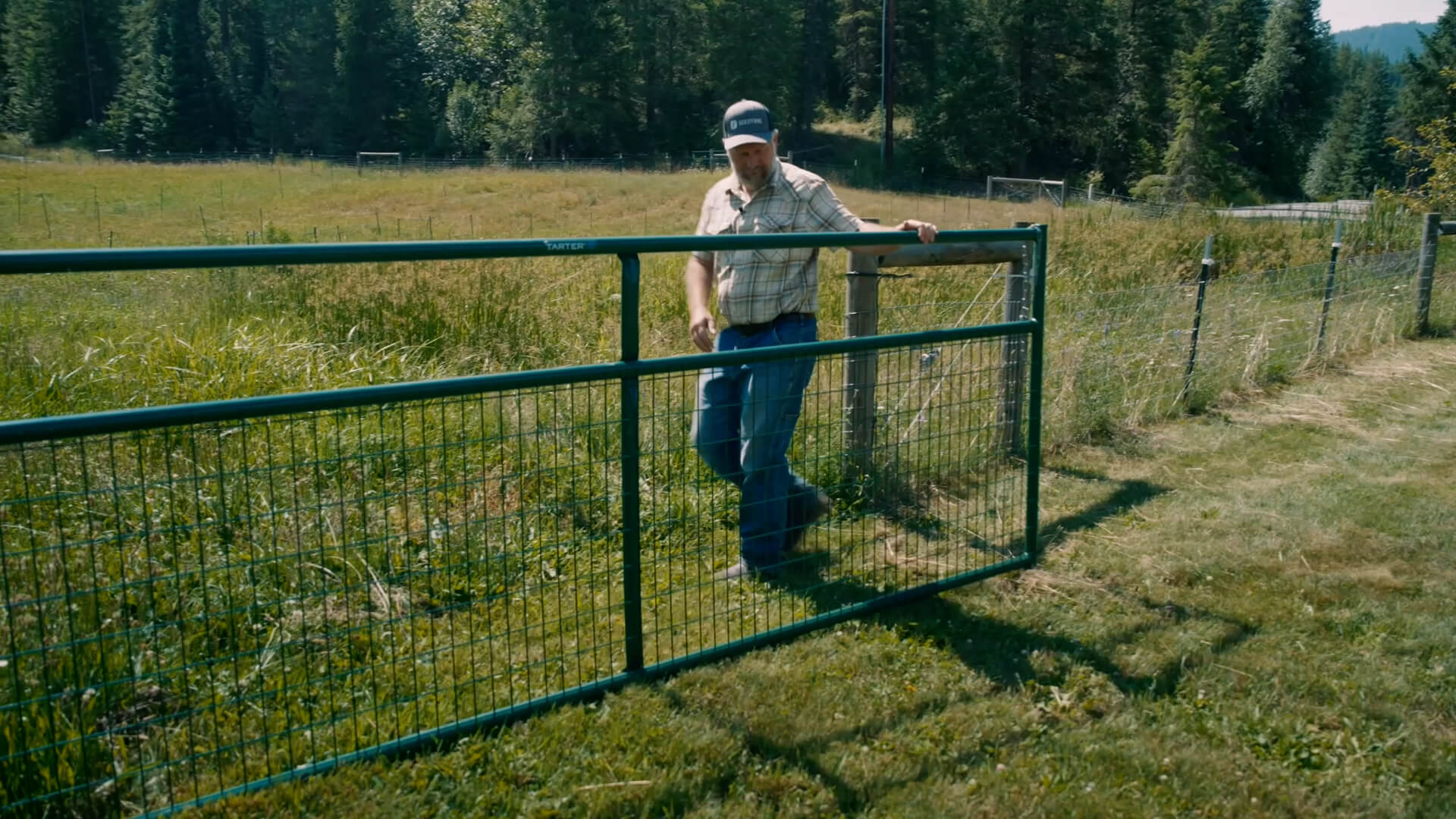 A man closing a gate in a pasture.