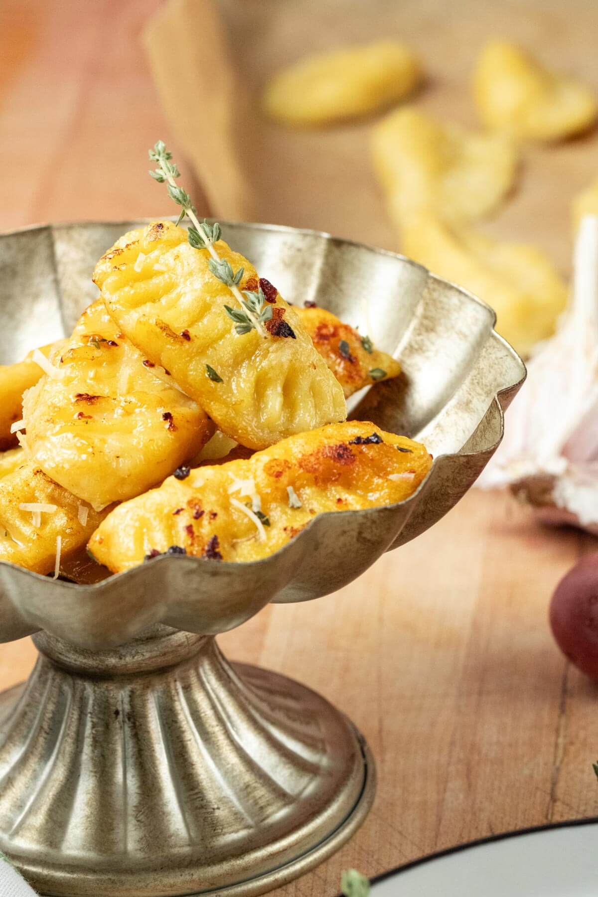 Homemade gnocchi garnished with fresh thyme served in a silver dish.