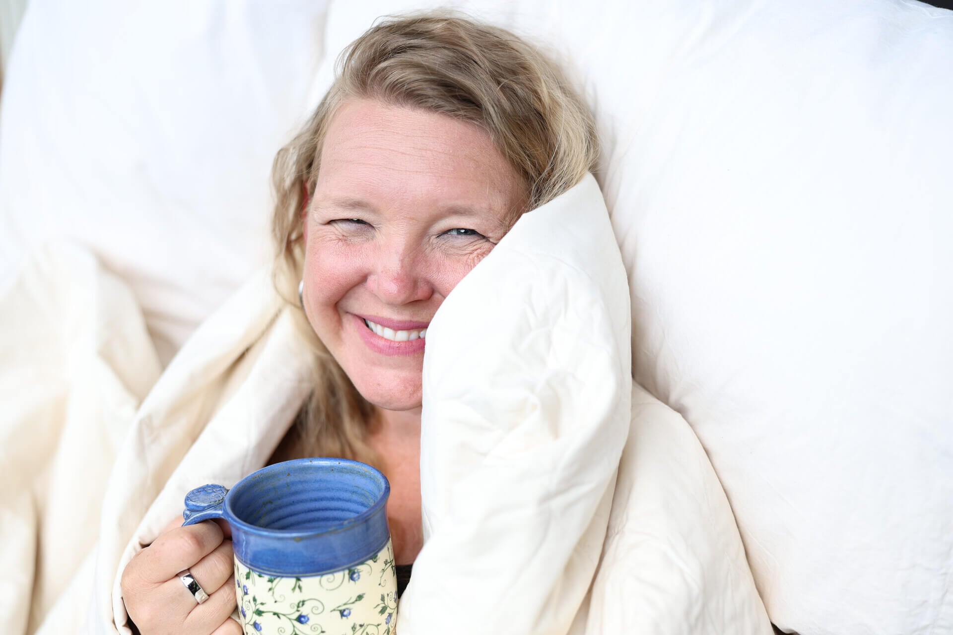A woman laying in bed with a cup of coffee.