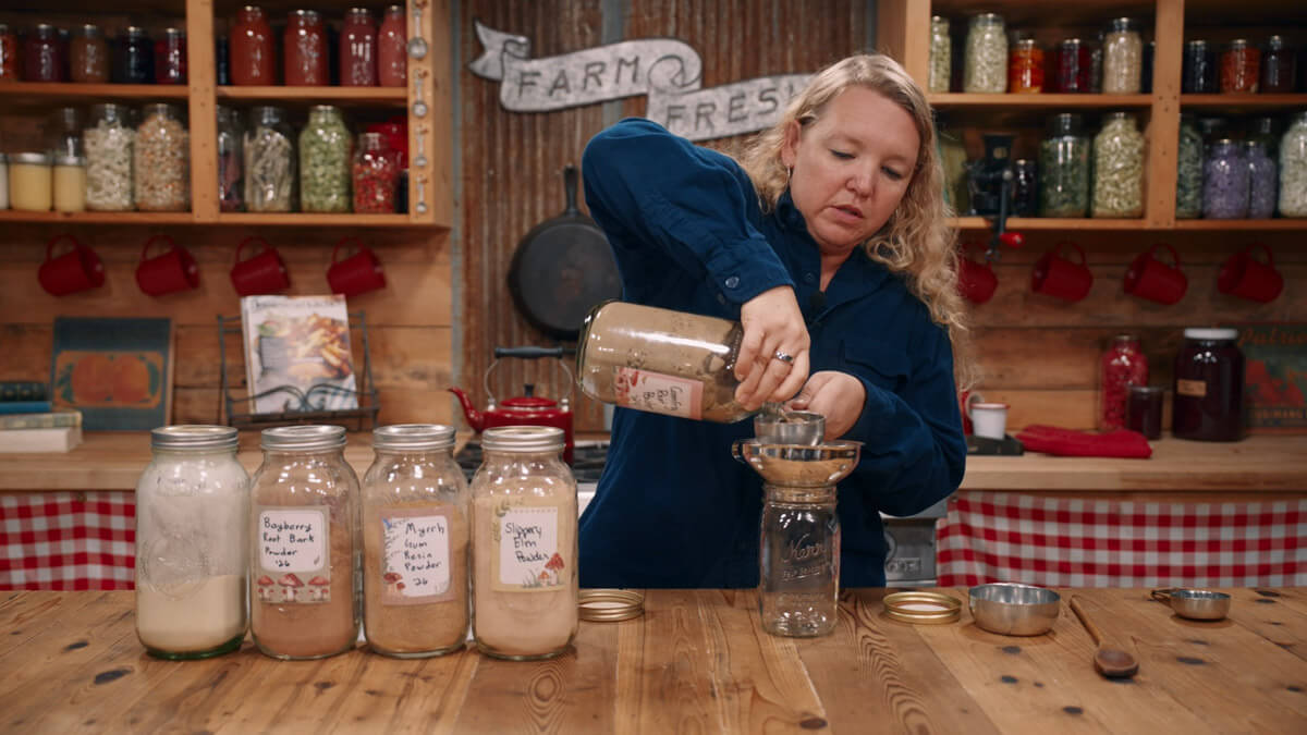 A woman measuring powdered herbs into a jar.