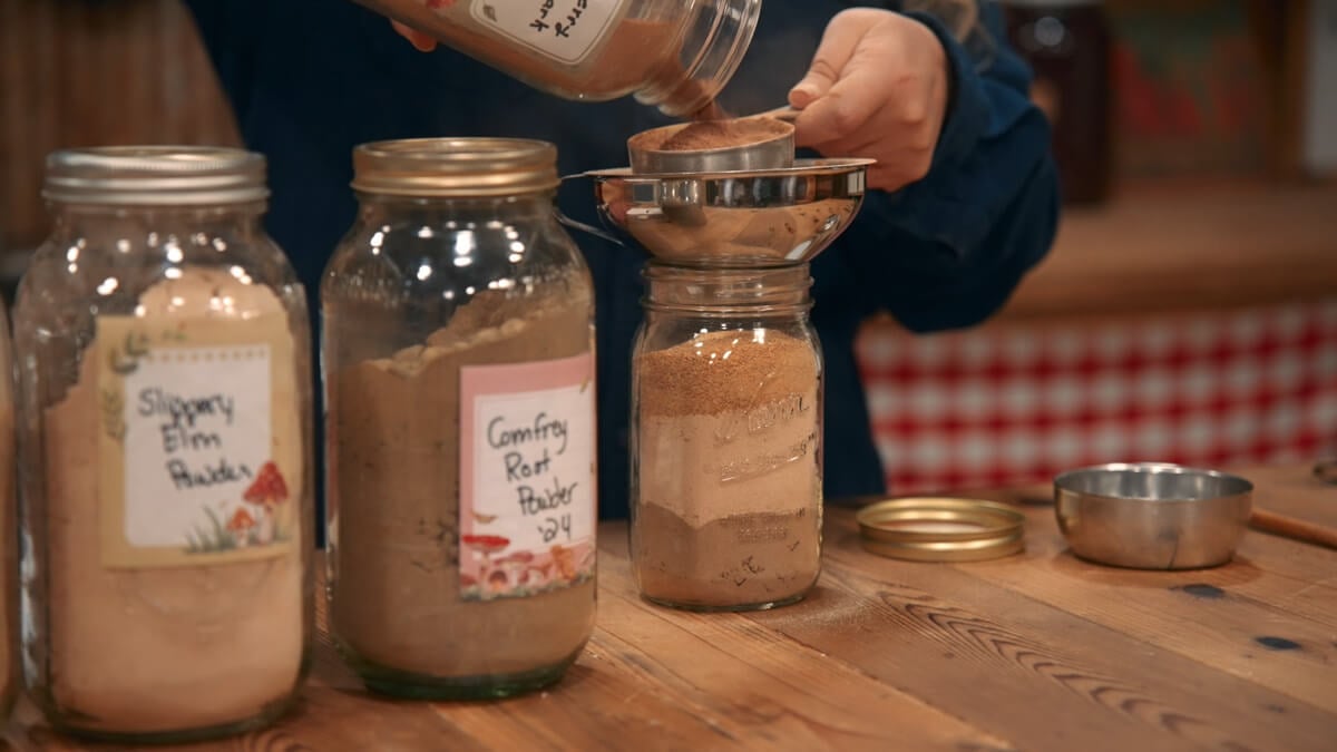 A woman measuring powdered herbs into a jar.