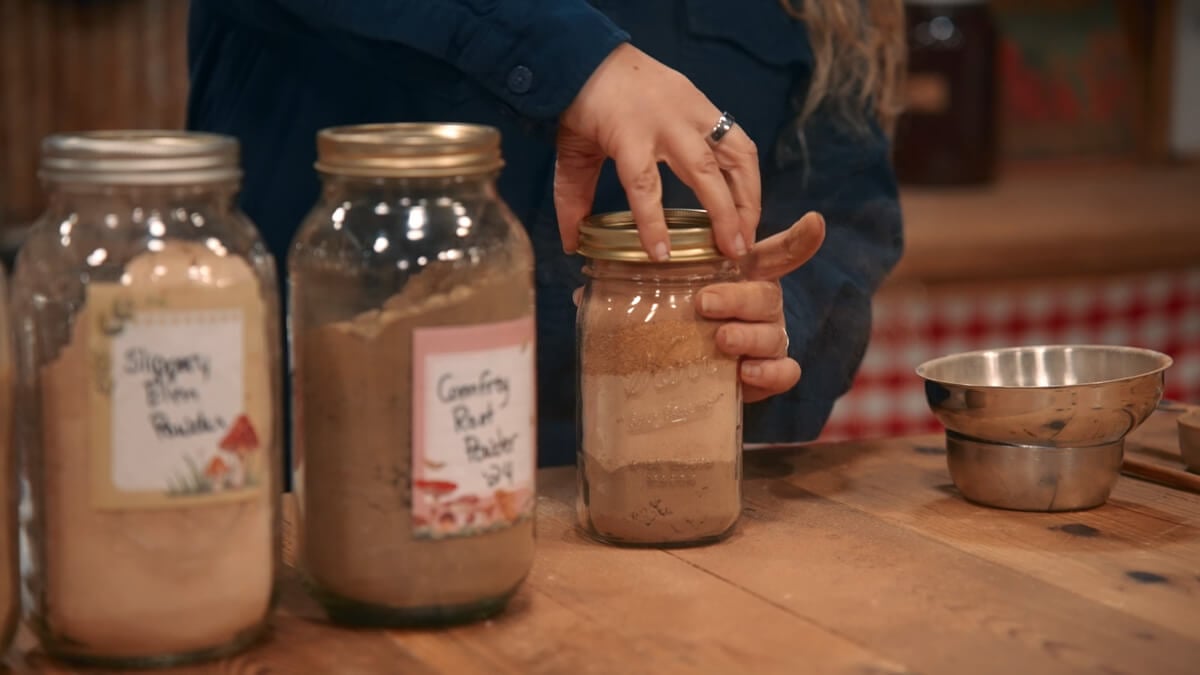 A woman adding a lid onto a Mason jar filled with medicinal herbs.