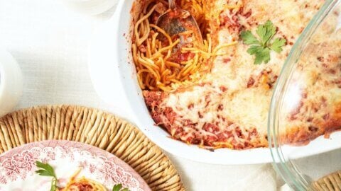 Bird's-eye view of a white plate with a serving of baked spaghetti sitting next to a casserole dish full of baked spaghetti.