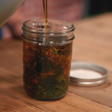 Pouring oil over dried herbs in a glass jar.