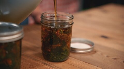 Pouring oil over dried herbs in a glass jar.